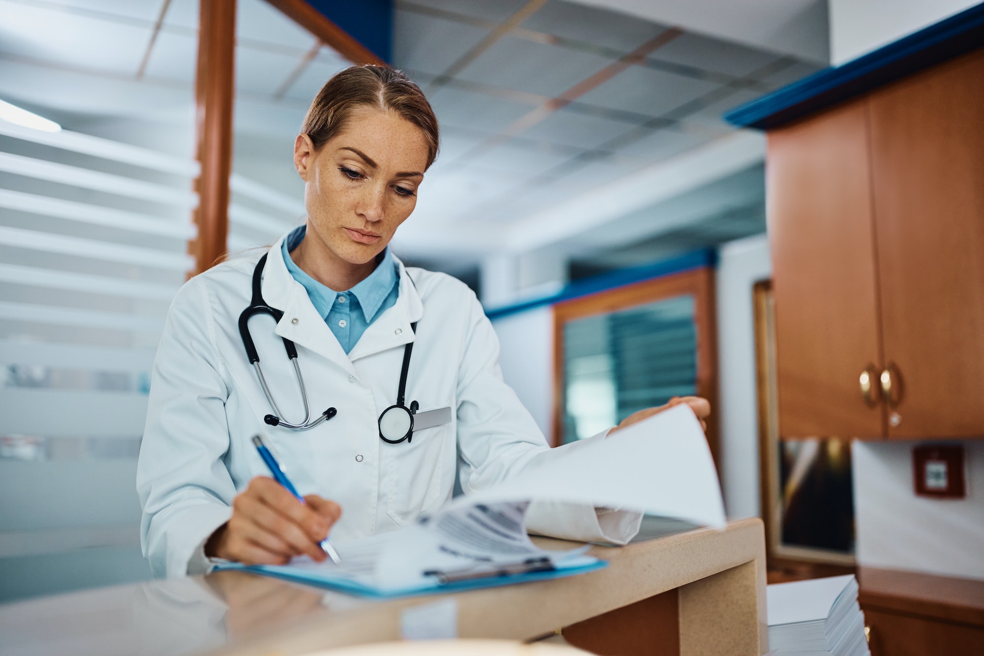 Female doctor writing medical reports at reception desk at medical clinic.